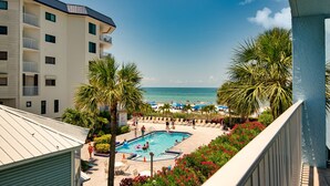 A pool area with a view of the ocean, surrounded by palm trees and lounge chairs. - Beachfront 3BR Condo with Oversized Gulf View Balcony, Pool and Spa (Indian Shores)