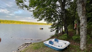 Un petit bateau sur une rive herbeuse, au bord d’un lac, avec des arbres et une ligne de côte lointaine.