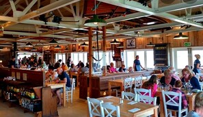 Guests can dine in a lively atmosphere with exposed beams, wooden tables, and framed artwork.