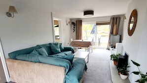 A spacious living room with a large sofa, a dining table, and a TV. - Property 5 Minutes Walk From Trearddur Bay Beach (Holyhead)