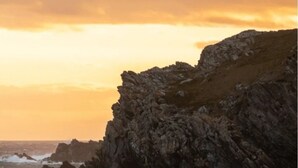 A rocky coastline with waves crashing against the shore and a person standing on the beach. - Property 5 Minutes Walk From Trearddur Bay Beach (Holyhead)