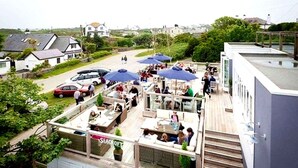 A rooftop bar with outdoor seating and umbrellas, overlooking a residential area with houses and a road. - Property 5 Minutes Walk From Trearddur Bay Beach (Holyhead)