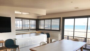A modern kitchen with a large island, bar stools, and a dining table with chairs. There are large windows with blinds, a view of the sea, and a flat-screen TV mounted on the wall. - Seafront -  feet in the sand - the most beautiful view of Narbonne Plage (Narbonne Plage)