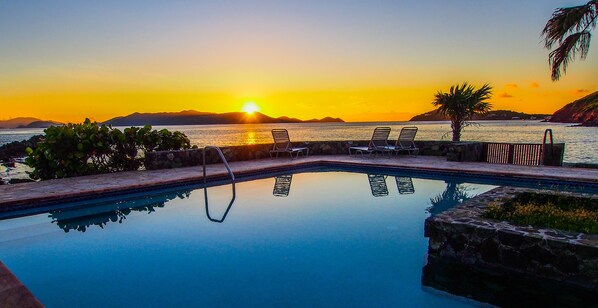 A pool with lounge chairs and a sunset view.