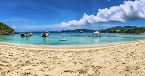 A beach with clear turquoise water, boats, and a white tent.