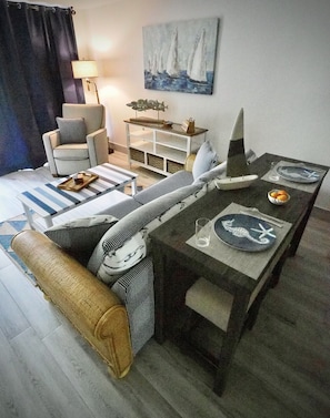 En moderne stue med en stribet sofa, et spisebord med tallerkener og en lille model af en sejlbåd, samt et maleri af sejlbåde på væggen.