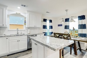 A kitchen with white cabinets, a granite countertop, and a dining area with a wooden table and chairs.