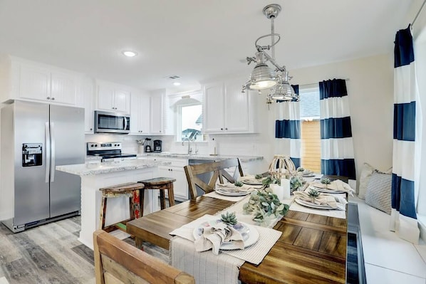 A modern kitchen with white cabinetry, stainless steel appliances, and a wooden dining table set for four.