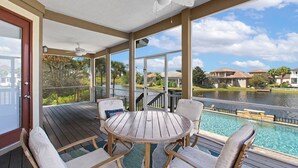 A covered outdoor area with a pool, wooden deck, and a view of a lake and houses in the background. - Siesta Del Sol- Lakefront, Destiny West, Private Pool, Tennis, Fitness! (Destin)