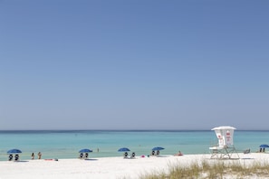 A beach with white sand, clear blue water, and a lifeguard tower.
