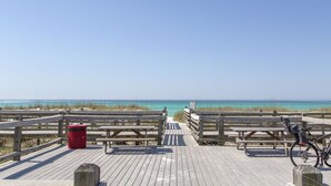 A wooden boardwalk with picnic tables and a bicycle, leading to a beach with clear blue water. - Siesta Del Sol- Lakefront, Destiny West, Private Pool, Tennis, Fitness! (Destin)