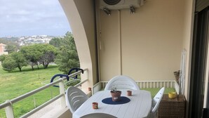 A balcony with a white table and chairs, a potted plant, and a view of greenery and houses. - Refúgio Ls (Guia)