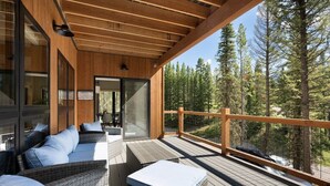 A wooden deck with outdoor seating and a view of a forest.
