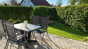 Un patio al aire libre con una mesa, sillas, una alfombra pequeña y una planta en maceta.