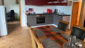 Una cocina compacta con armarios rojos, una mesa de comedor con cojines a rayas y una cafetera.