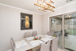 A dining area with a table set for six, a framed pineapple artwork, and a sliding glass door leading to an outdoor patio.