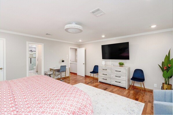 Une chambre moderne avec un grand lit, un bureau, une commode et un téléviseur fixé au mur.