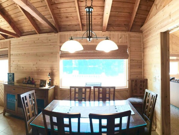 Cozy cabin interior with a dining area, high ceiling, and large window.