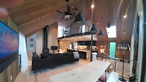 A spacious living area with a high ceiling, a large sofa, a dining table, and a kitchen in the background. - This deluxe modern new 3-story home with central AC offers the best of Bozeman! (Bozeman)