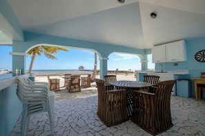 Un patio frente a la playa con comedor, cocina y vista al océano.