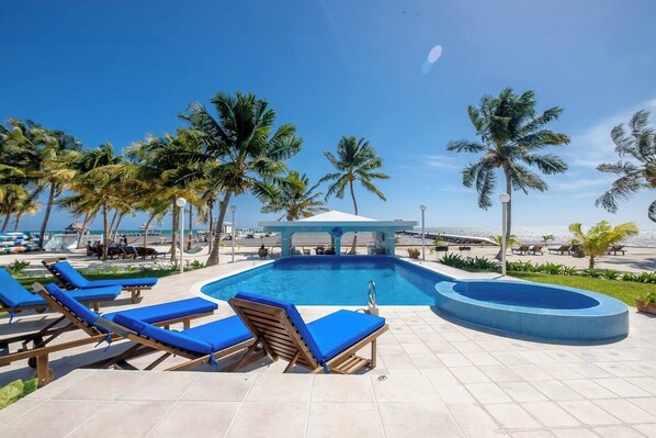 Un área de piscina con sillas reclinables azules, una piscina pequeña y palmeras.