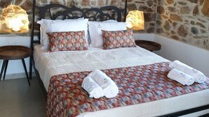 A bedroom with a stone wall, a bed with patterned bedding, and a chandelier.