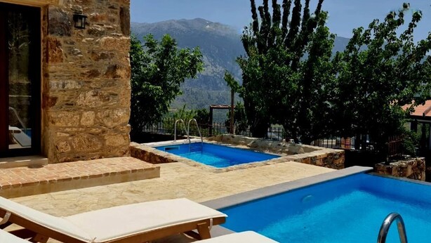 A pool area with lounge chairs, a stone building, and a mountain view.
