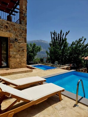Un área de piscina con sillas de descanso, un edificio de piedra y vistas a la montaña.