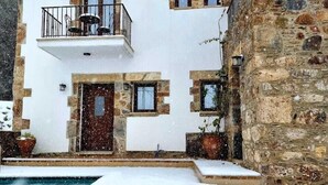 A two-story building with a stone facade, a balcony with outdoor furniture, and a swimming pool partially covered in snow.