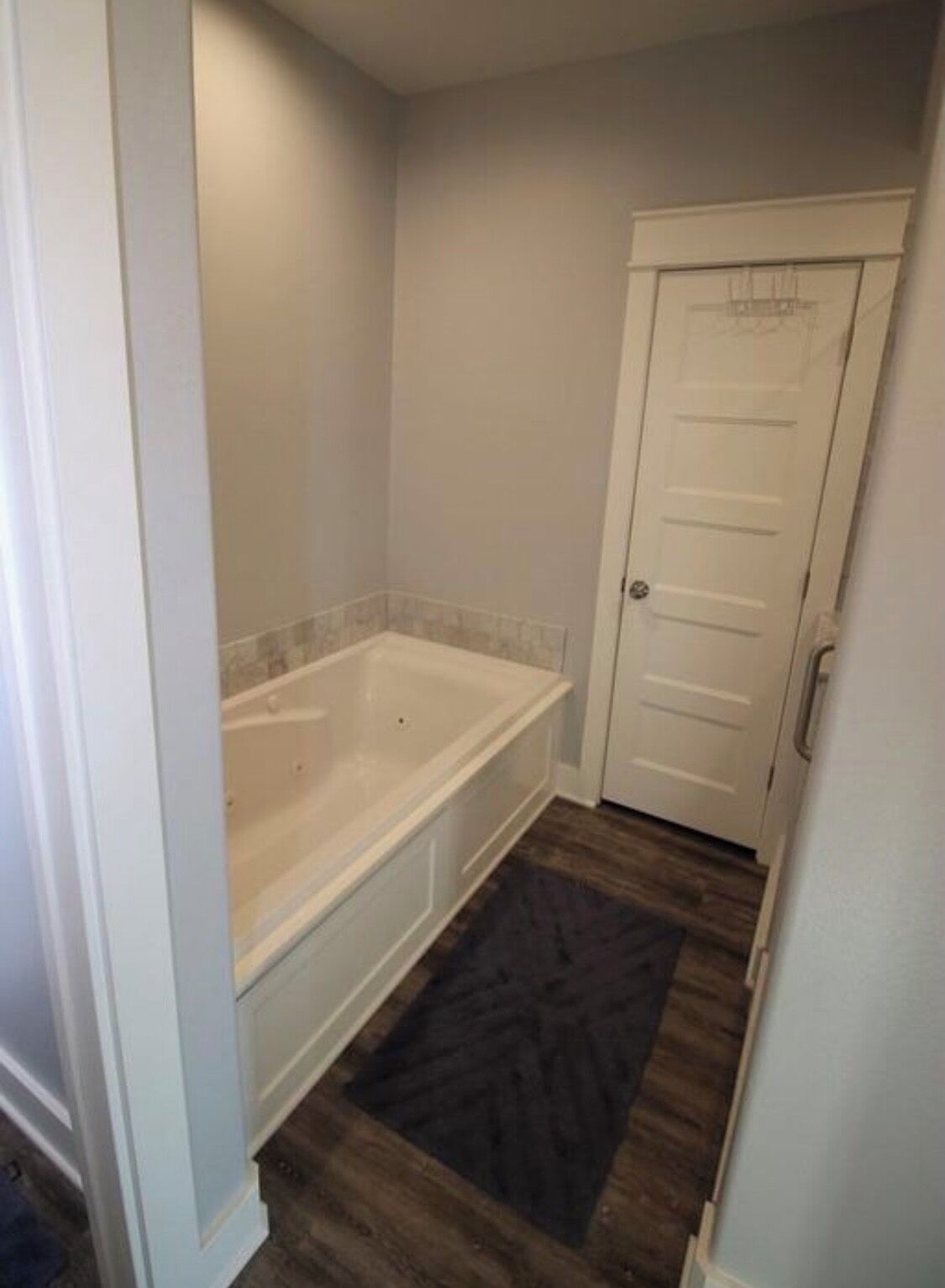 Un baño con bañera, una puerta y una alfombra oscura en el suelo.