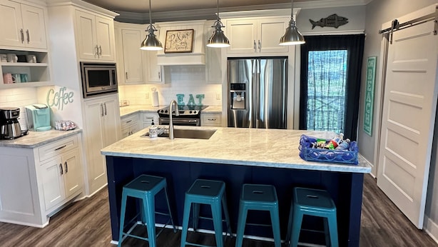 Una cocina moderna con armarios blancos, una isla grande con taburetes de bar, electrodomésticos de acero inoxidable e iluminación colgante.