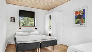 Une chambre à coucher moderne avec un lit, une fenêtre donnant sur des arbres, une armoire et une œuvre d’art encadrée accrochée au mur.