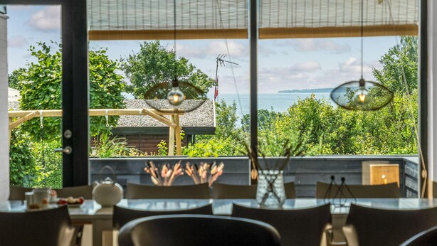 Un espace repas offrant une vue sur un jardin et un plan d’eau.