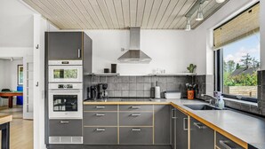 Une cuisine moderne dotée d’un îlot central, d’appareils électroménagers intégrés et d’une grande fenêtre offrant une vue sur l’extérieur.