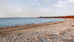 Une plage de galets bordée par une mer calme et des collines lointaines.