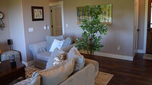 A living room with a grey sofa, a small table, a plant, and a painting on the wall.