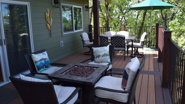 A covered outdoor deck with wicker furniture, a table with a mosaic top, and a green umbrella.