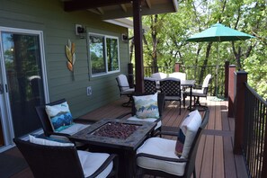 A covered outdoor deck with wicker furniture, a table with a mosaic top, and a green umbrella.