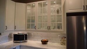 A kitchen with white cabinets, a stainless steel microwave, and a fruit bowl on the counter.