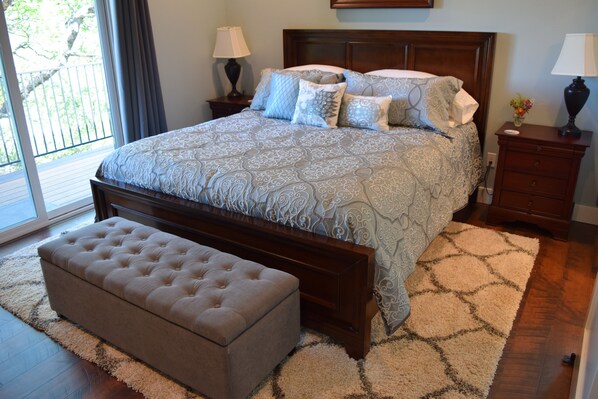 A bedroom with a large bed, a wooden headboard, two bedside tables with lamps, a bench, and a view of the outdoors.