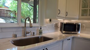 A kitchen with white cabinets, a stainless steel sink, a faucet, a microwave, and a window with a view of greenery outside.