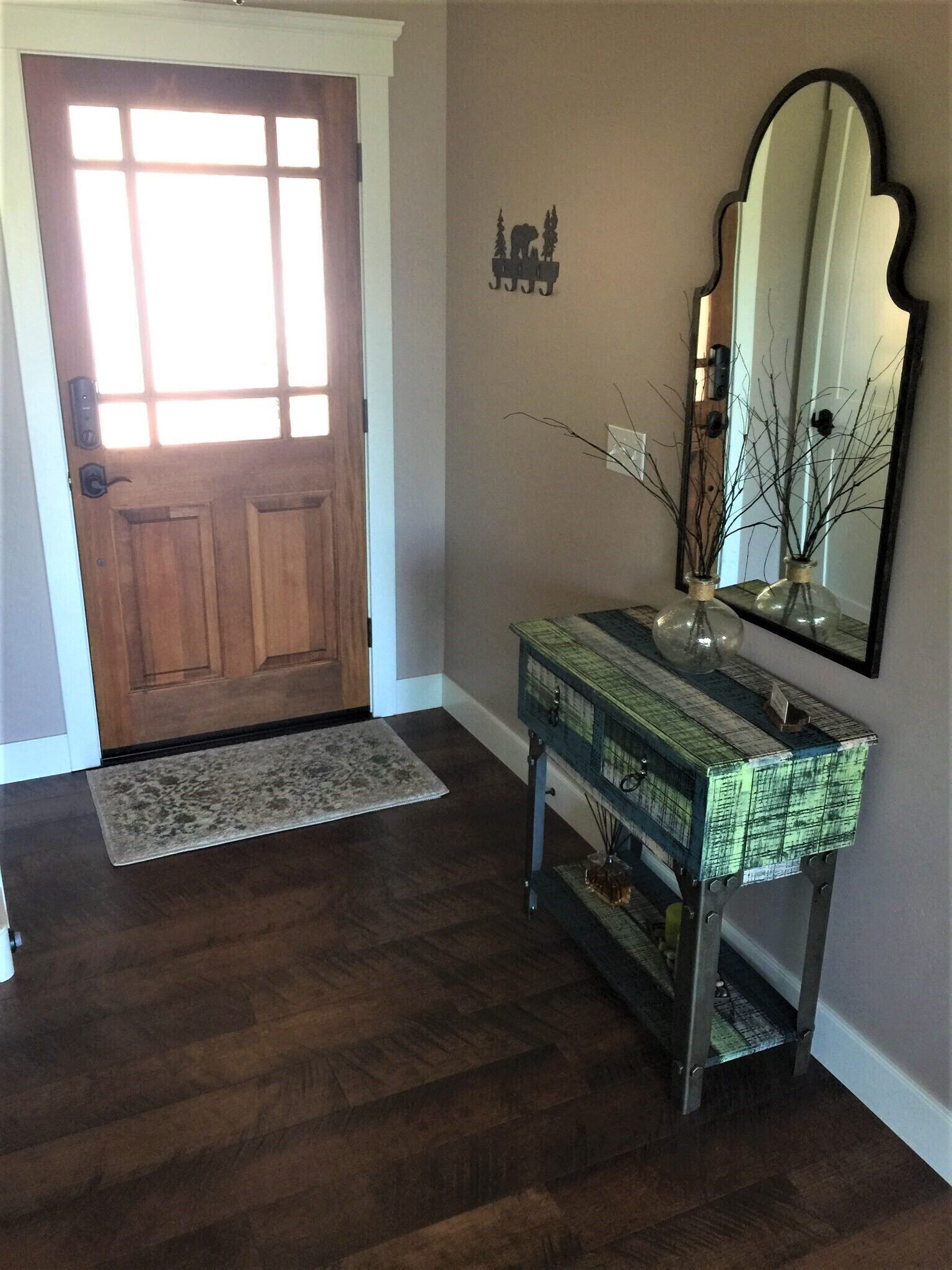 Une porte en bois avec un panneau de verre, une console ornée de divers objets décoratifs et un grand miroir accroché au mur.