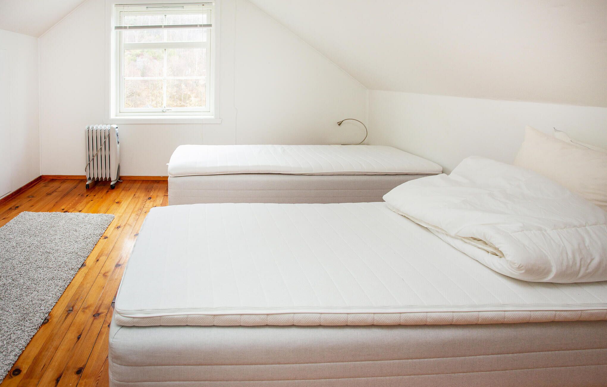 A bedroom with a sloped ceiling, a radiator, a window, and a gray rug.