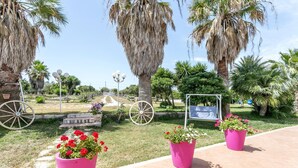 A garden with palm trees, a swing, and flower pots.