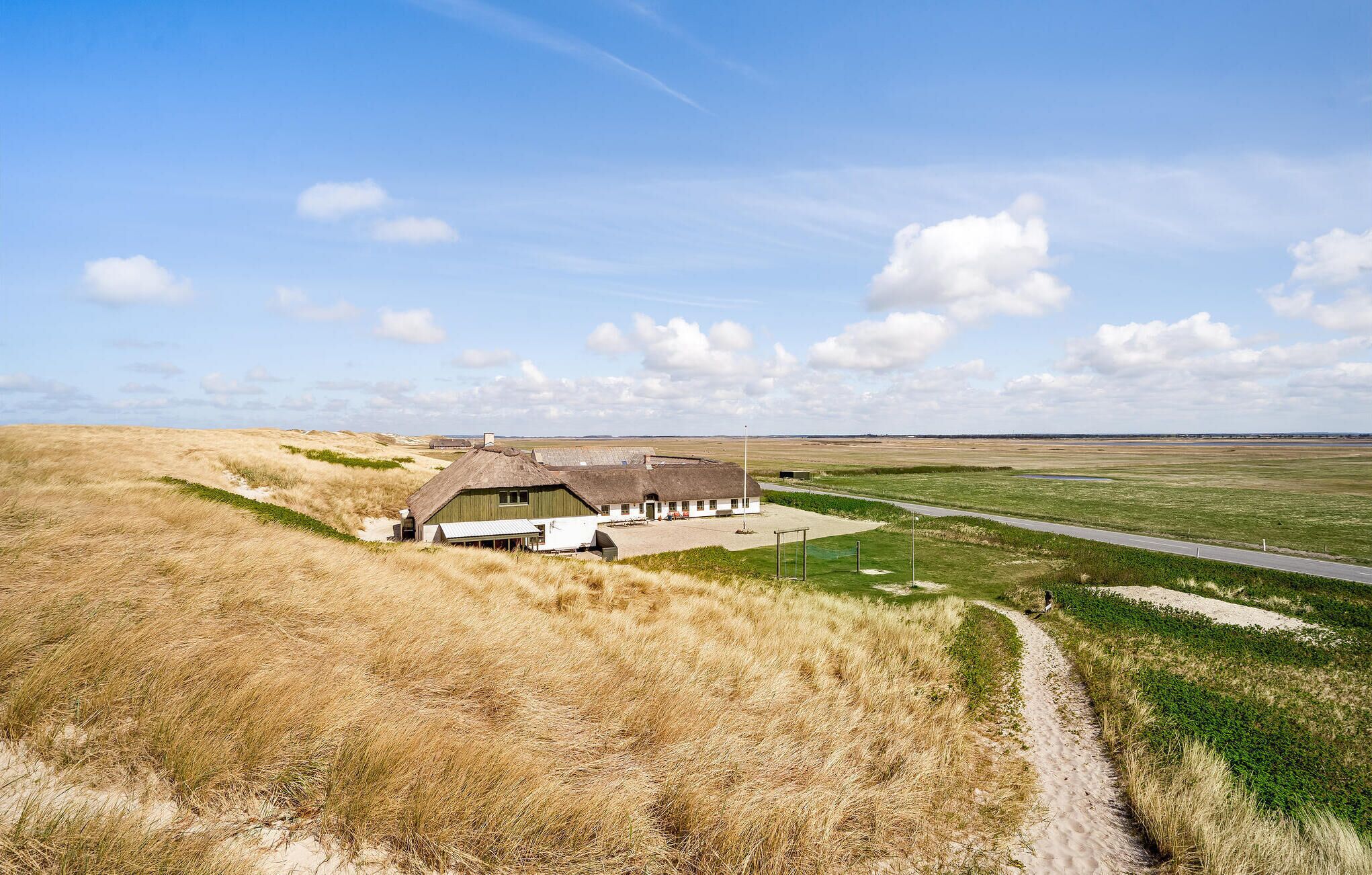 A building with a thatched roof and a solar panel array, surrounded by open fields and a clear sky.