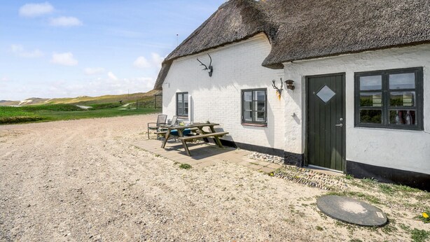 Een wit gebouw met rieten dak, een grindpad en een picknicktafel buiten.
