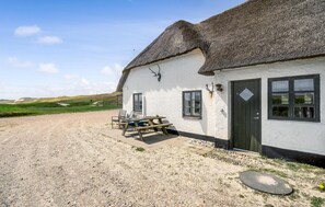 A white building with a thatched roof, a gravel driveway, and a picnic table outside.