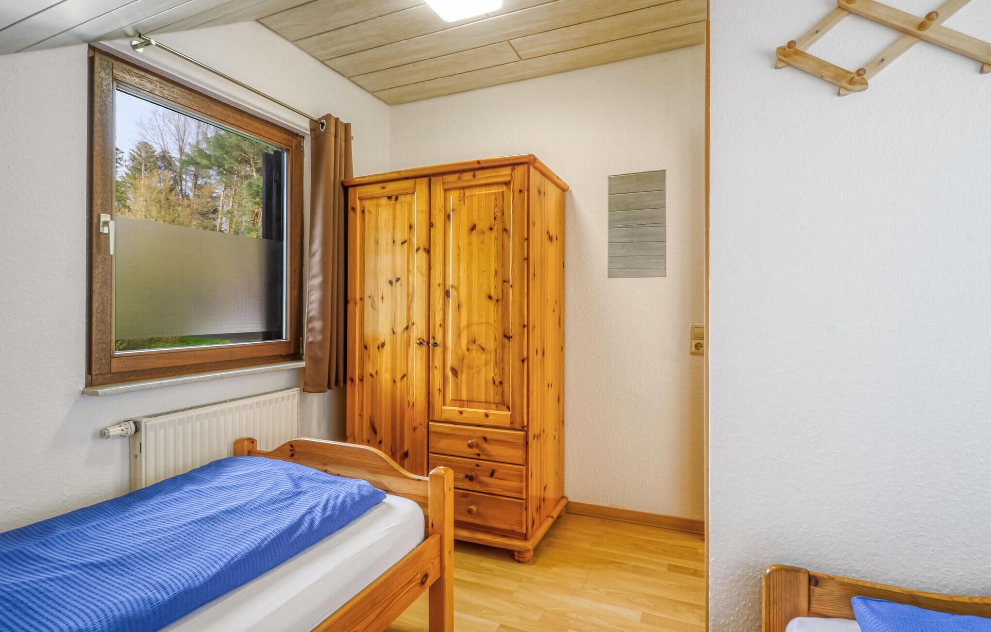 A small, tidy room with a single bed, a wooden wardrobe, a window with curtains, and a radiator.