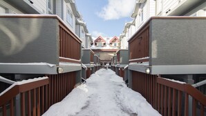 Un chemin enneigé entre des bâtiments dotés de balcons en bois, sous un ciel dégagé.