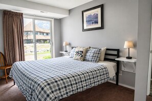 Un dormitorio con una cama grande, dos mesitas de noche con lámparas, una ventana con cortinas y un cuadro enmarcado en la pared.